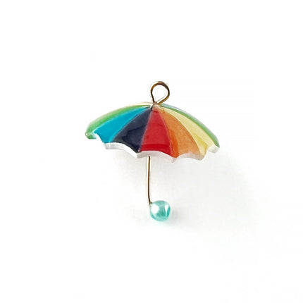 A miniature beach umbrella charm with a rainbow of coloured panels in green, blue, purple, red, orange, and yellow, featuring a gold-tone metal frame and a small light blue bead at the bottom.