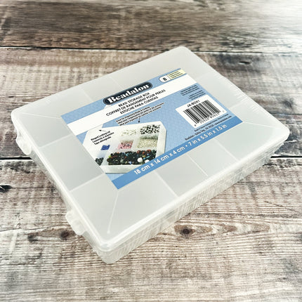 A clear plastic bead organizer box with a blue and white label, photographed on a rustic wood surface.