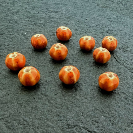 Ten small round orange beads with a textured, spotted pattern and a central hole, arranged on a dark gray slate surface.