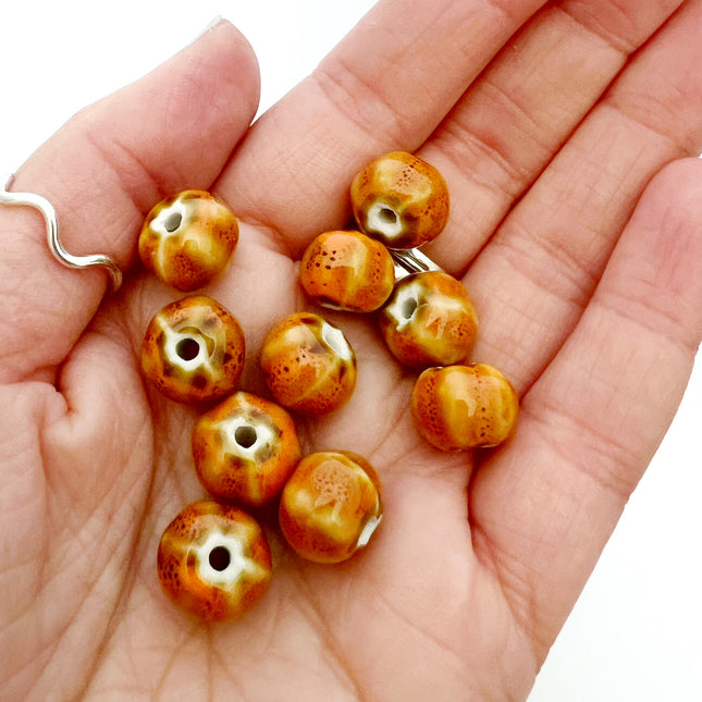 Ten small round ceramic beads with a marbled orange, brown, and cream pattern, held in the palm of a hand.