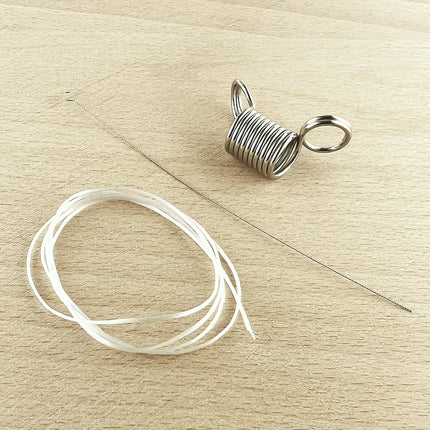 A silver metal spring bead stopper, shown next to a coiled length of clear elastic cord and a flexible beading needle on a light wood background.