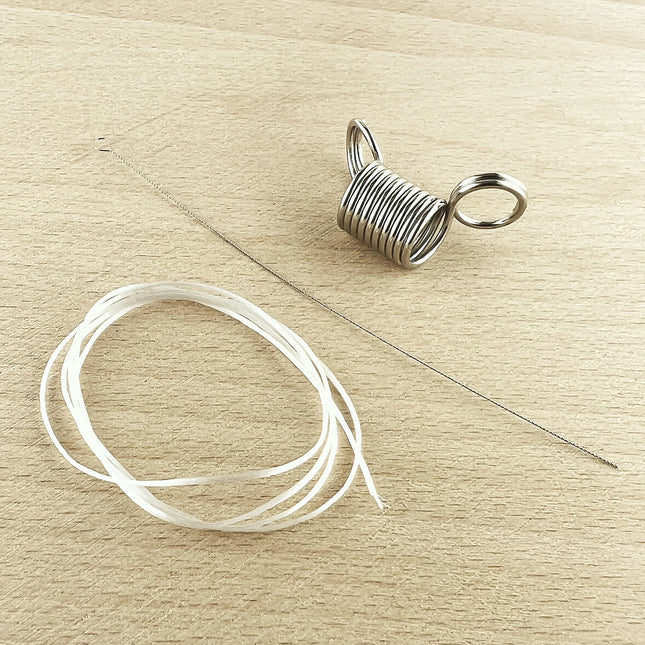 A silver metal spring bead stopper, shown next to a coiled length of clear elastic cord and a flexible beading needle on a light wood background.