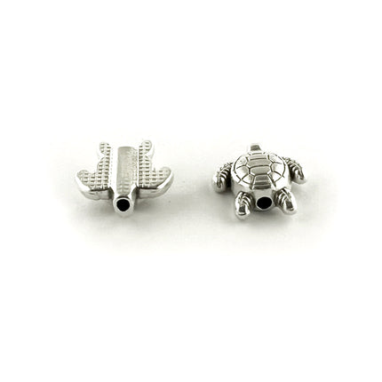 Two small silver-toned metal beads, shaped like a turtle, one is showing the top and the other the underneath of teh bead, shown on a plain white background.