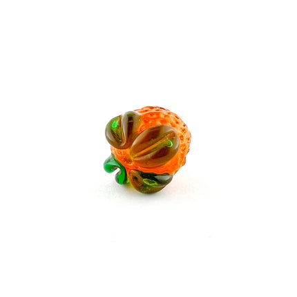 A small decorative glass bead shaped like an orange, featuring a textured orange body with green leaves.