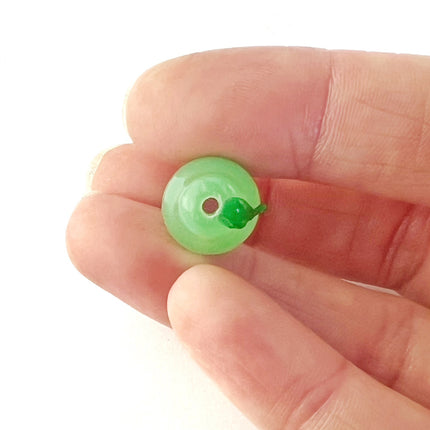 A view from the top of the pear bead showing the central hole and a tiny green leaf detail, held between a person's fingers against a white background.