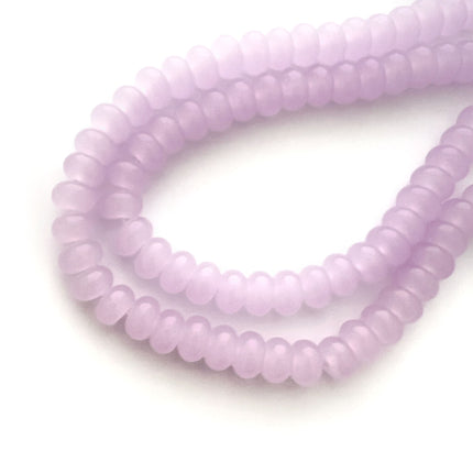 A close-up of a strand of small, round lavender beads on a plain white background.