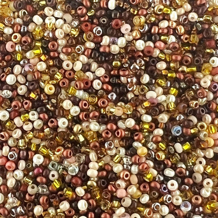 A close-up, top-down view of a dense pile of small round craft beads in assorted colors and finishes, including metallic rose gold, copper, bronze, gold, cream, and dark brown.