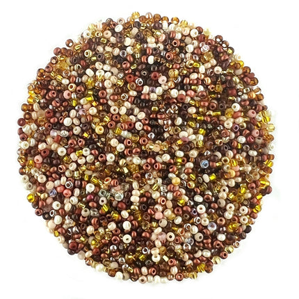 A circular pile of mixed seed beads in various colors including brown, bronze, gold, cream, and white, photographed on a solid white background.