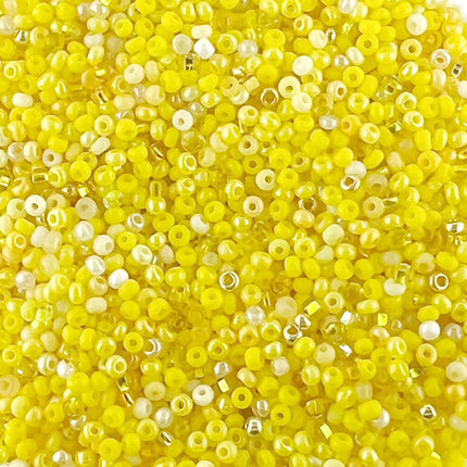A close-up pile of small round seeb beads in bright yellow, translucent yellow, and white.