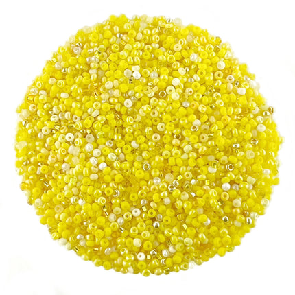 A pile of small round craft beads in bright yellow with some translucent white beads, arranged in a circular mound on a plain white background.