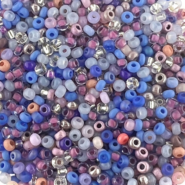 A dense pile of small seed beads in assorted pastel and metallic colours, including blue, pink, lavender, purple, peach, and silver.
